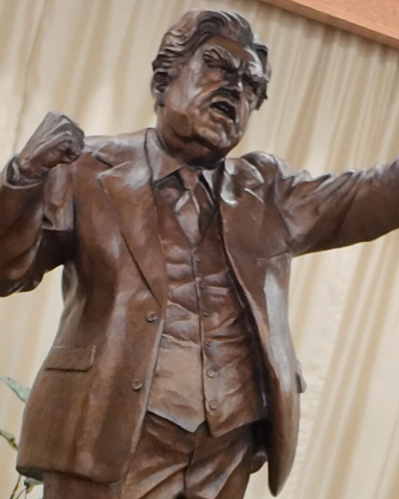Bronze statue of a man in a suit, yelling with clenched fist and outstretched arm.