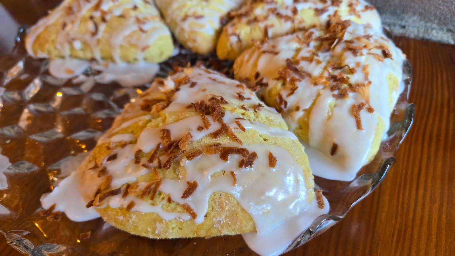Coconut scones, frosted with white glaze and toasted coconut, arranged on a glass plate.