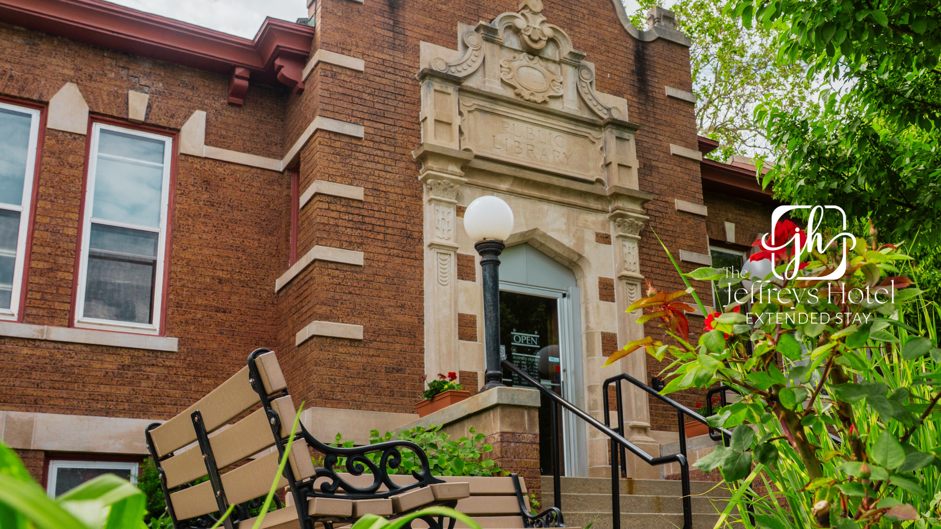 Brick building entrance to Osceola Public Library with light-colored trim and a wrought-iron bench in front. Green foliage surrounds the building.
