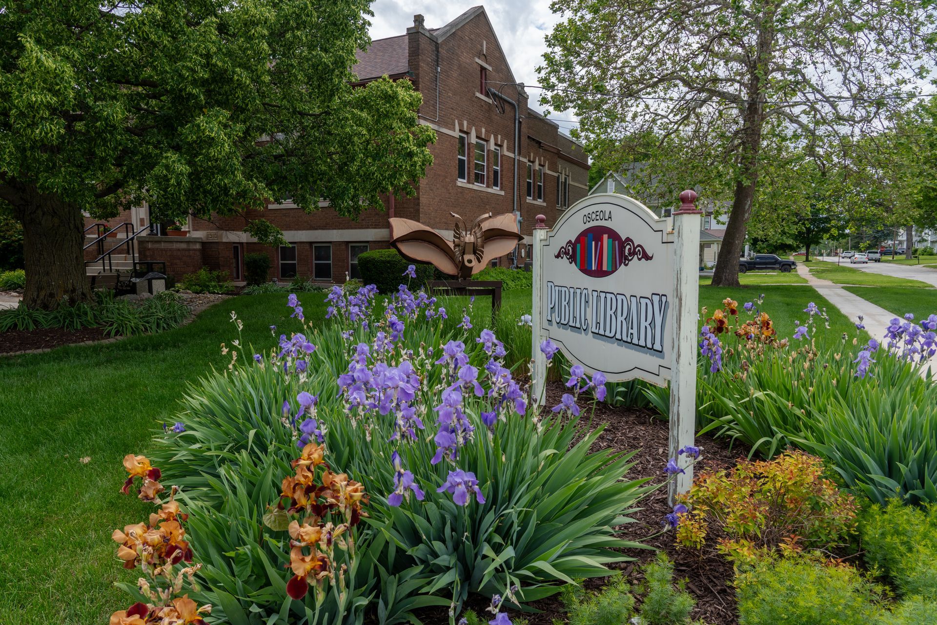 Exterior of the Osceola Public Library in Iowa, featuring a flower-filled garden with blooming irises.
