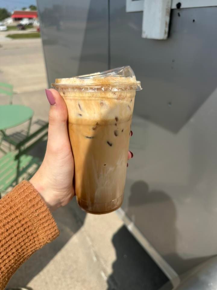 Hand holding an iced coffee with layers of coffee and cream in a clear cup.