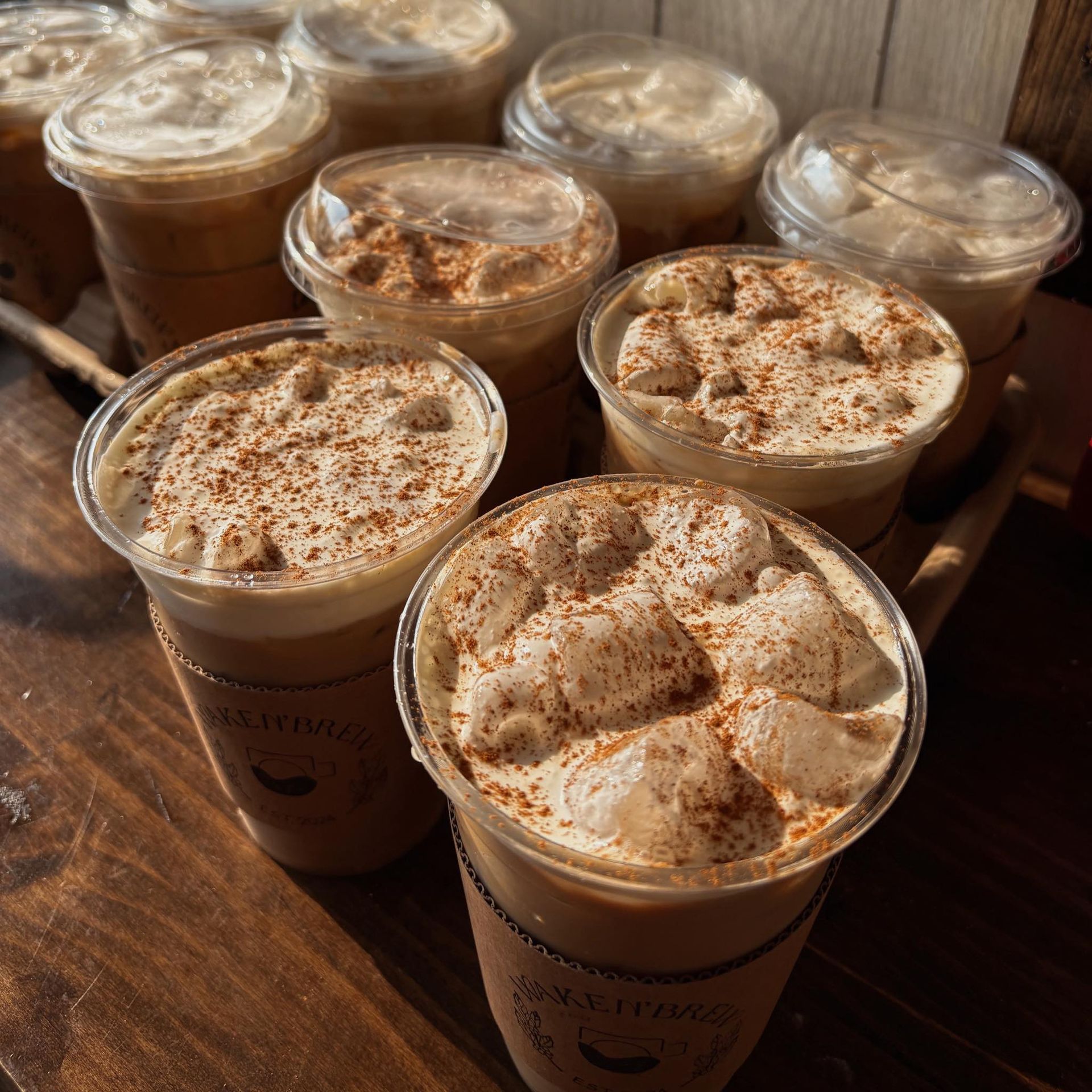 Iced coffee drinks topped with foam and cinnamon, in clear plastic cups on a wooden surface.