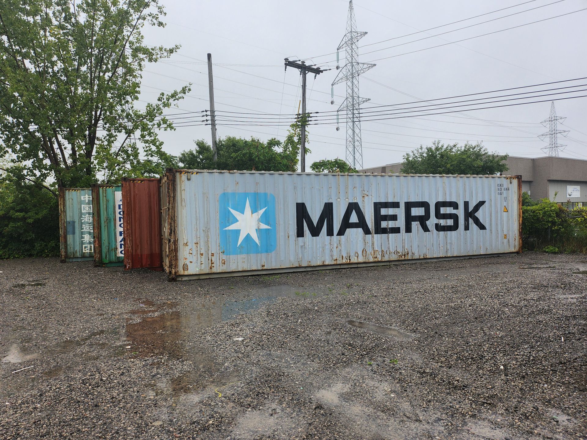 Un conteneur d'expédition Maersk est assis dans un terrain en gravier.