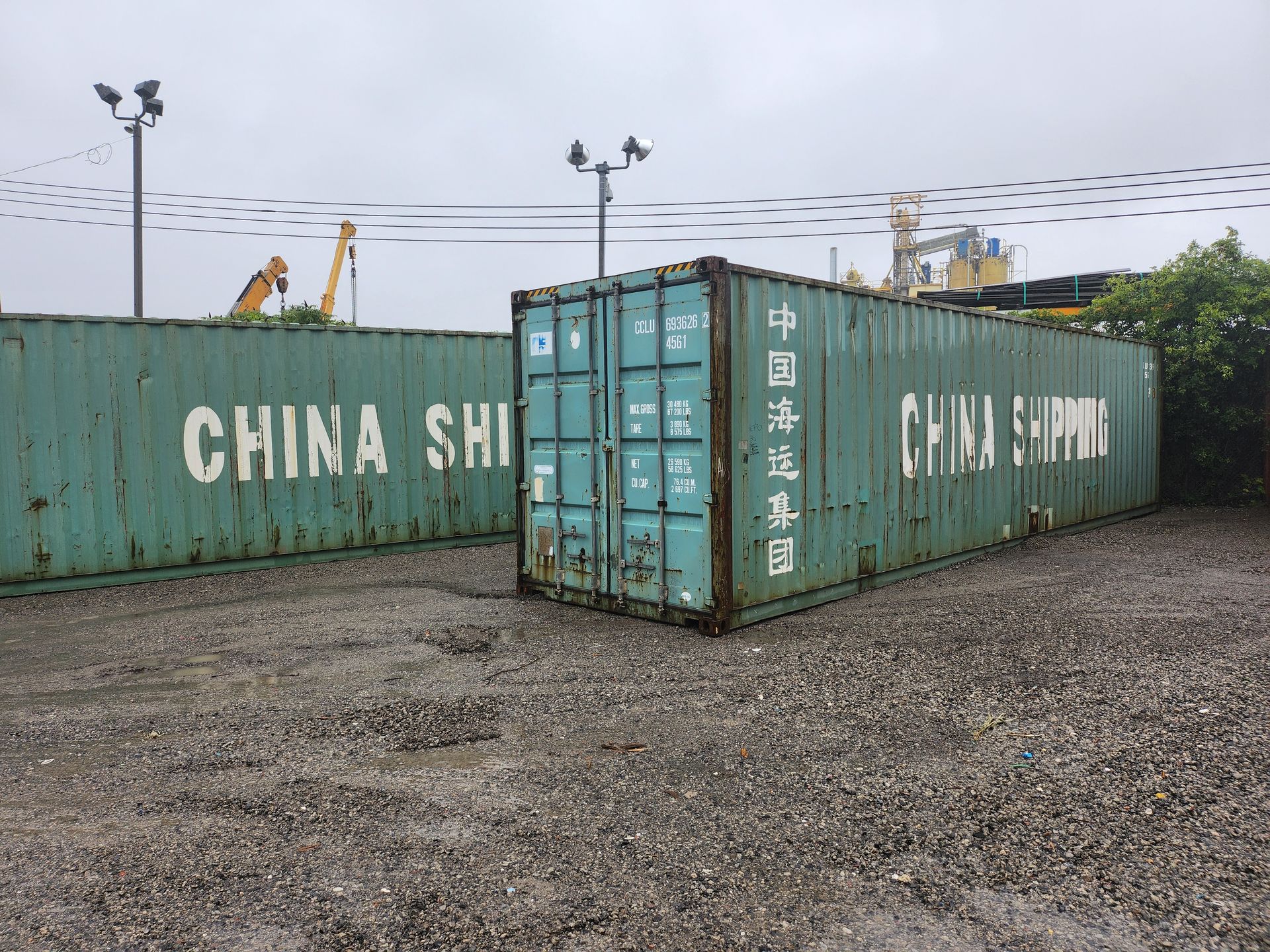 Deux conteneurs d'expédition sont assis l'un à côté de l'autre dans une zone de gravier.