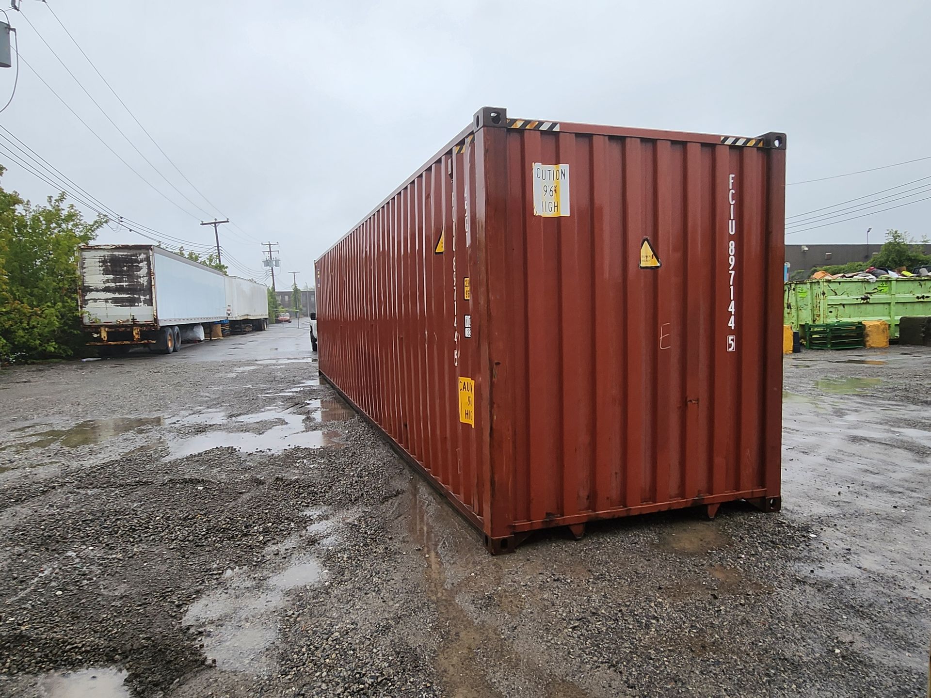 Un conteneur d'expédition rouge est garé sur un terrain en gravier