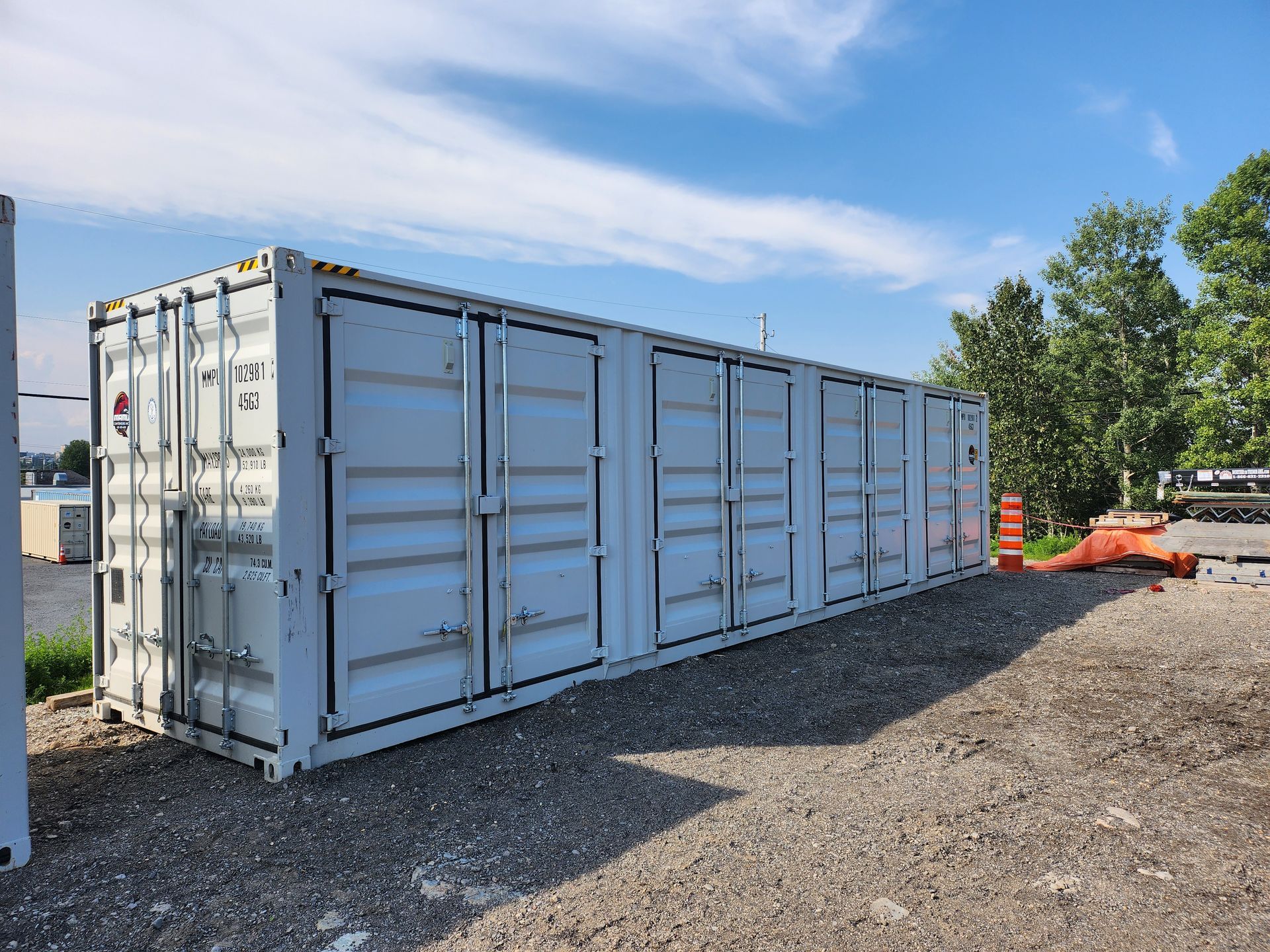 Un grand conteneur d'expédition blanc se trouve sur un terrain en gravier.