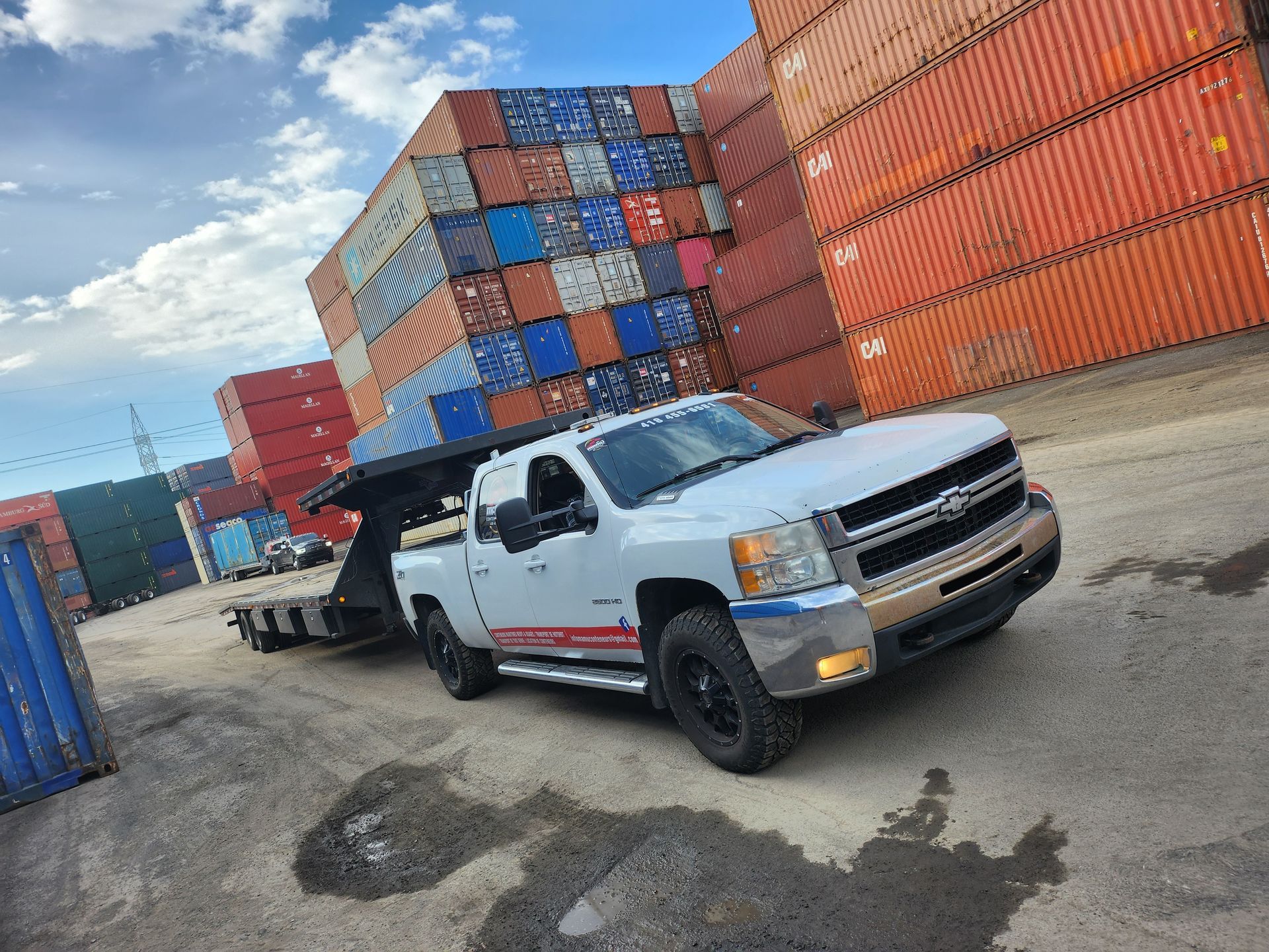 Un camion blanc tracte une remorque devant une pile de conteneurs d'expédition.