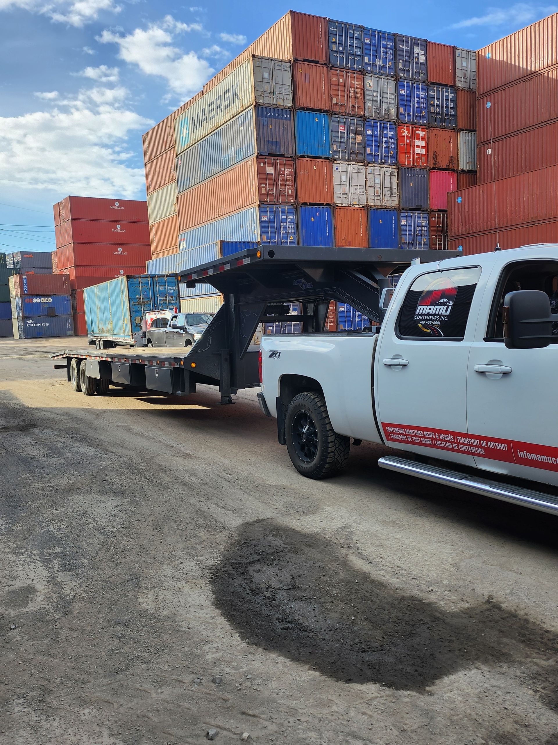 Un camion blanc tracte une remorque avec des piles de conteneurs d'expédition en arrière-plan.