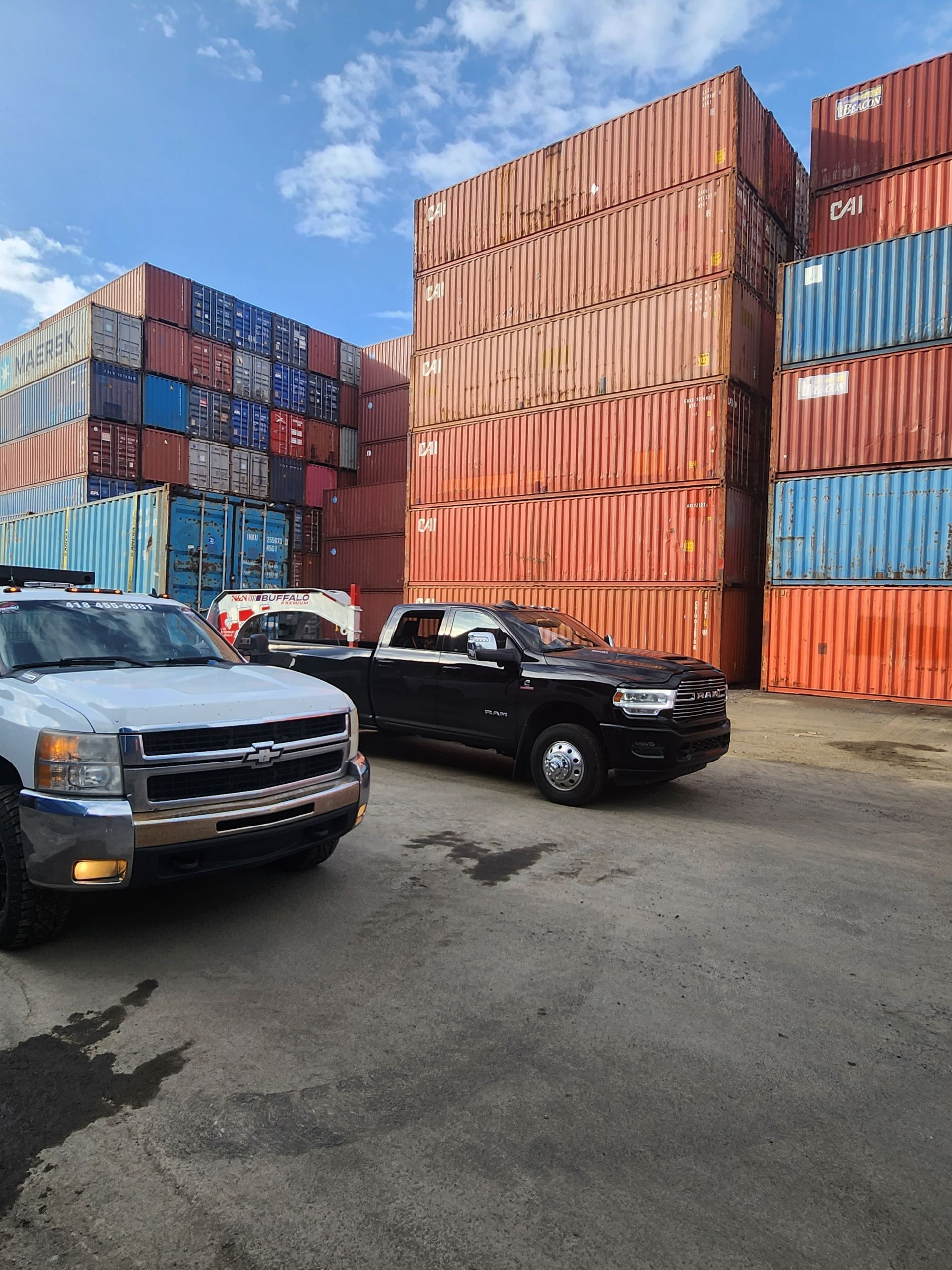 Deux camions sont garés devant une pile de conteneurs maritimes.