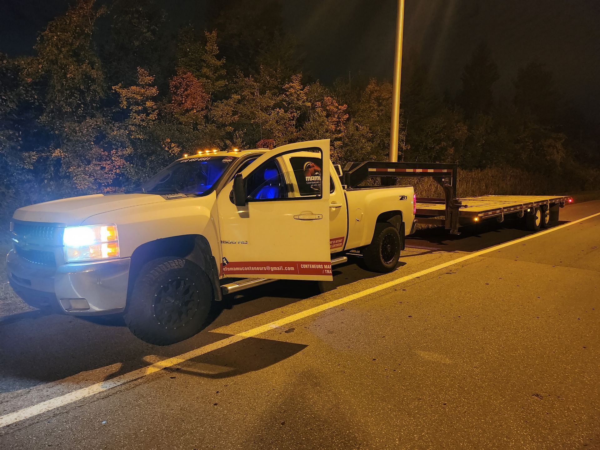 Une dépanneuse blanche est garée sur le bord de la route la nuit.