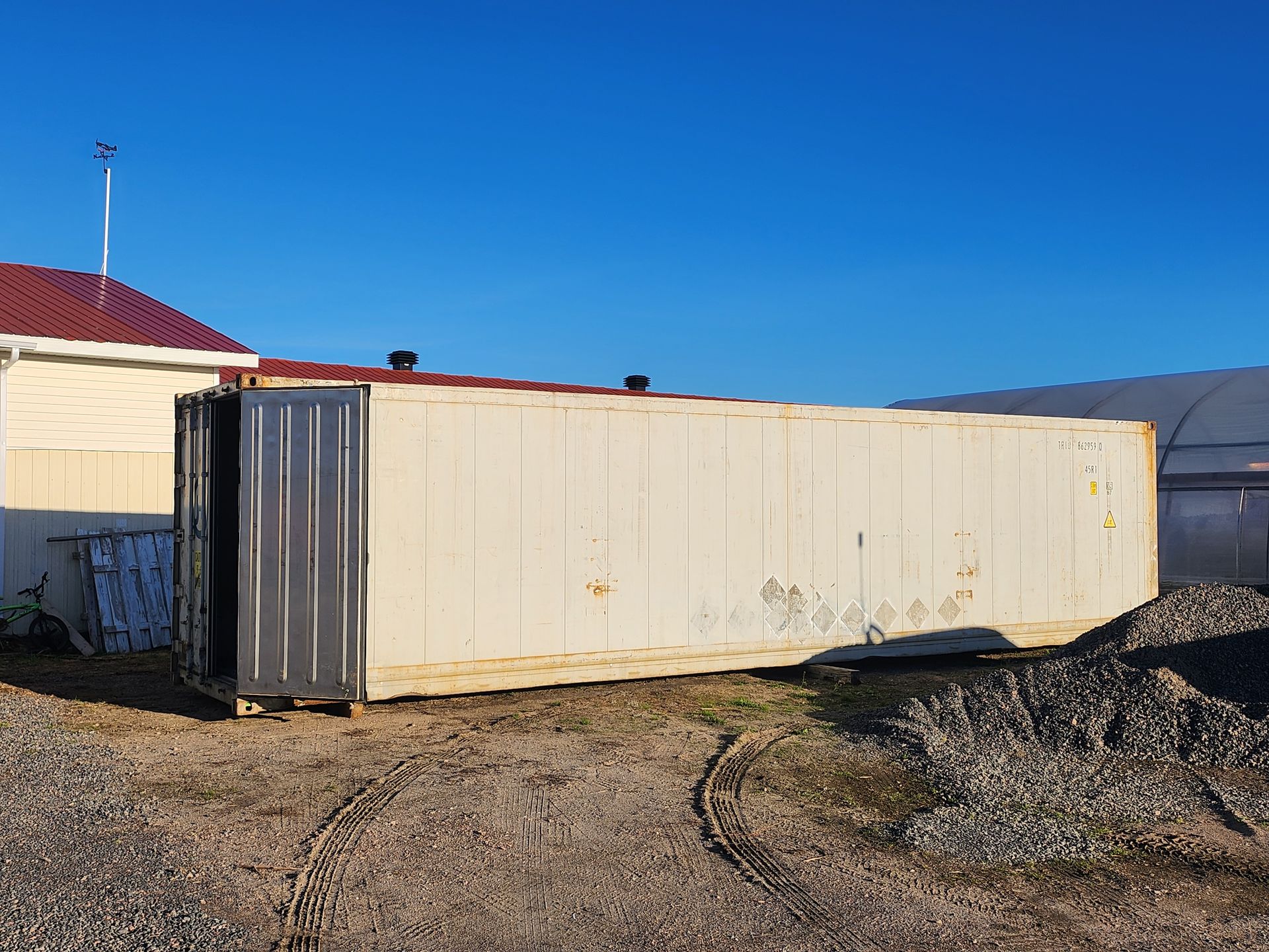Un grand conteneur d'expédition blanc est posé dans la terre devant une maison.