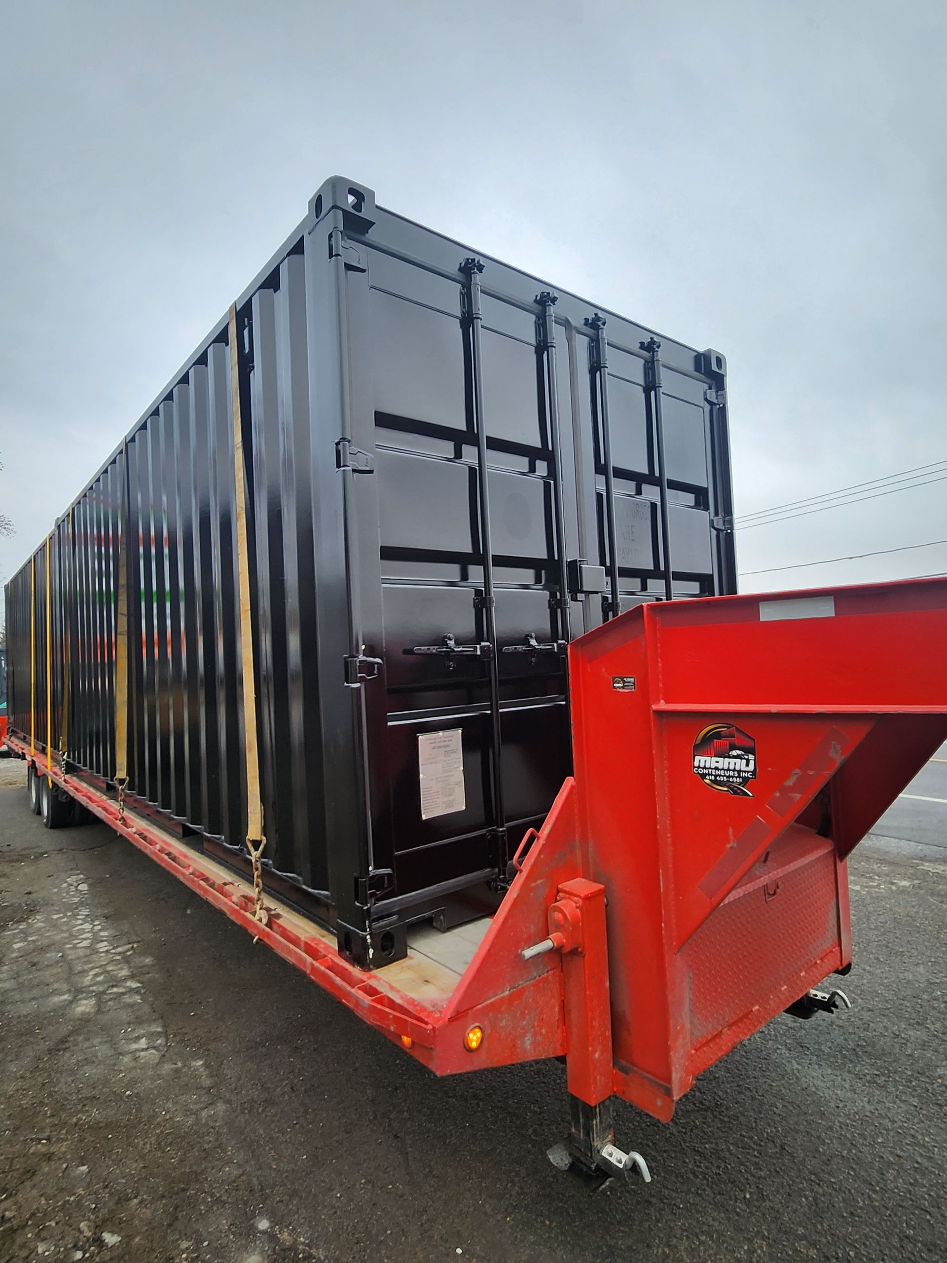 Un conteneur d'expédition noir est posé sur une remorque rouge.