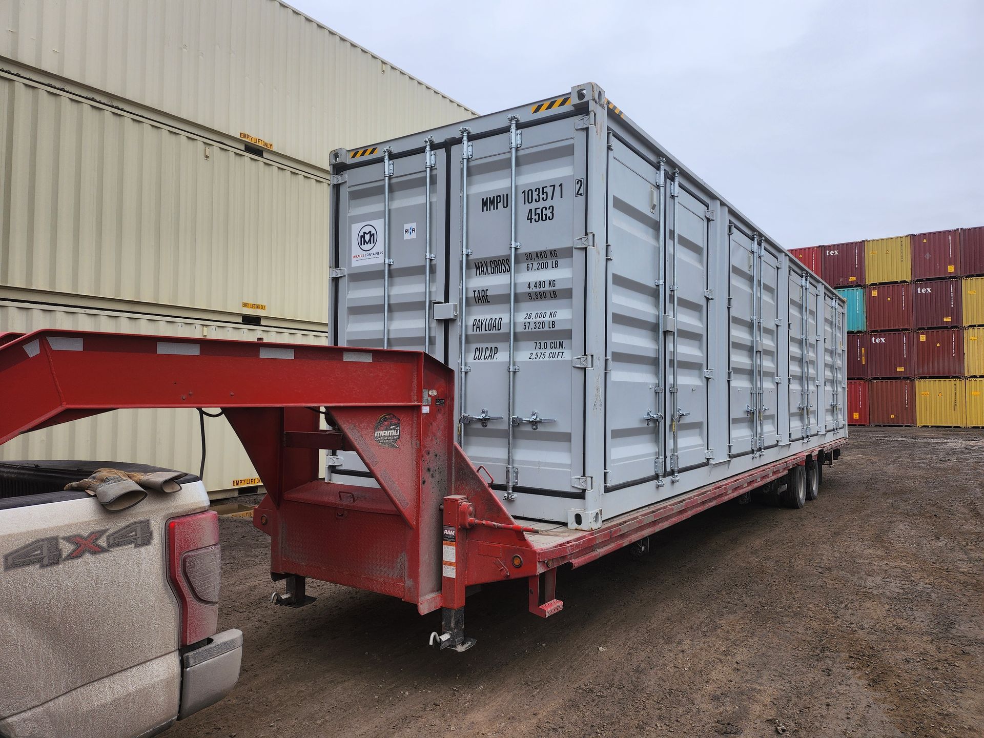 Un conteneur d'expédition sur une remorque est garé devant une rangée de conteneurs d'expédition.