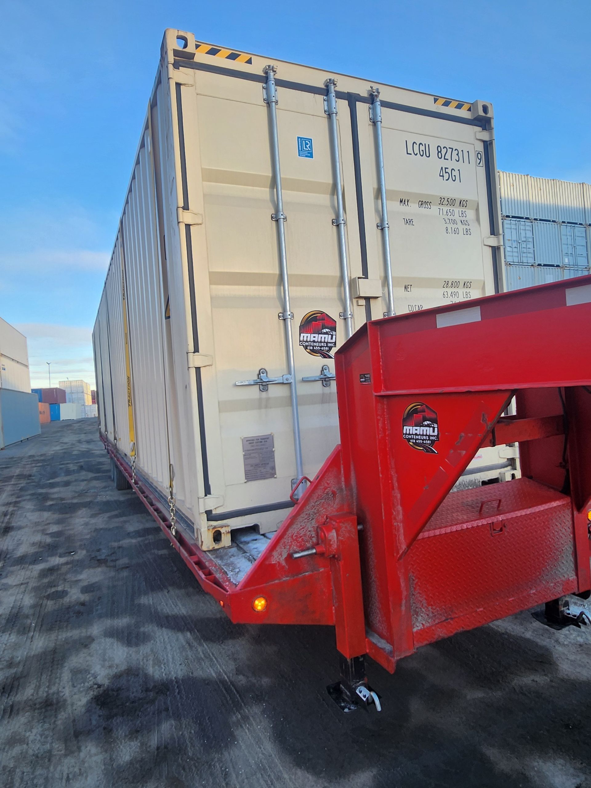 Un conteneur d'expédition blanc est remorqué par une remorque rouge.