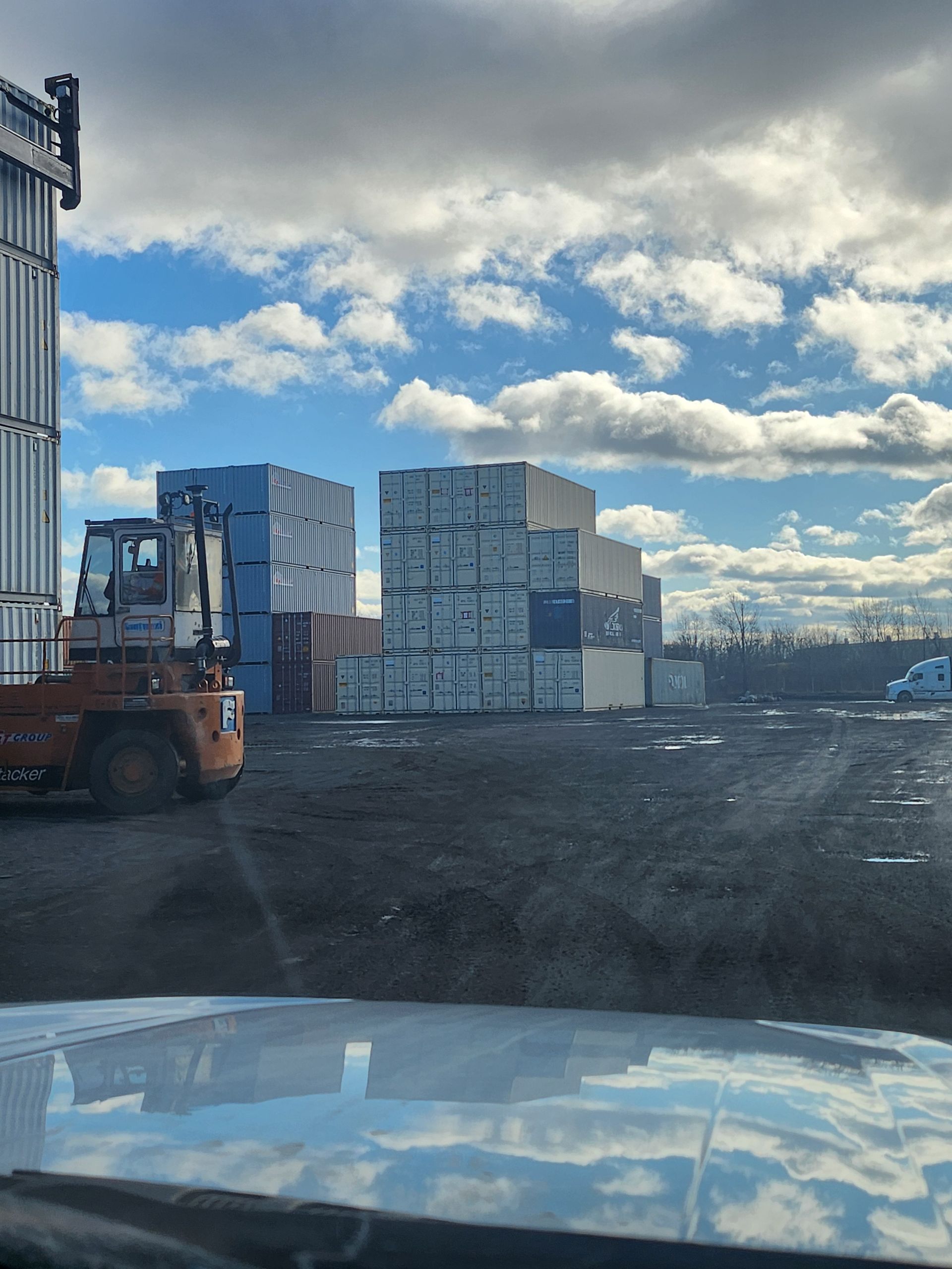 Un chariot élévateur déplace des piles de cartons dans un parking
