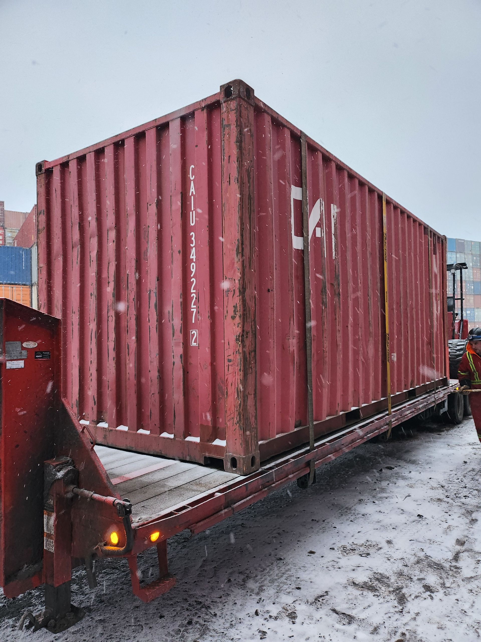 Un conteneur d'expédition rouge est posé sur une remorque dans la neige.