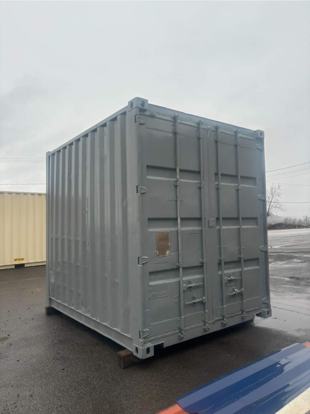 Un grand conteneur d'expédition gris est garé sur un parking.