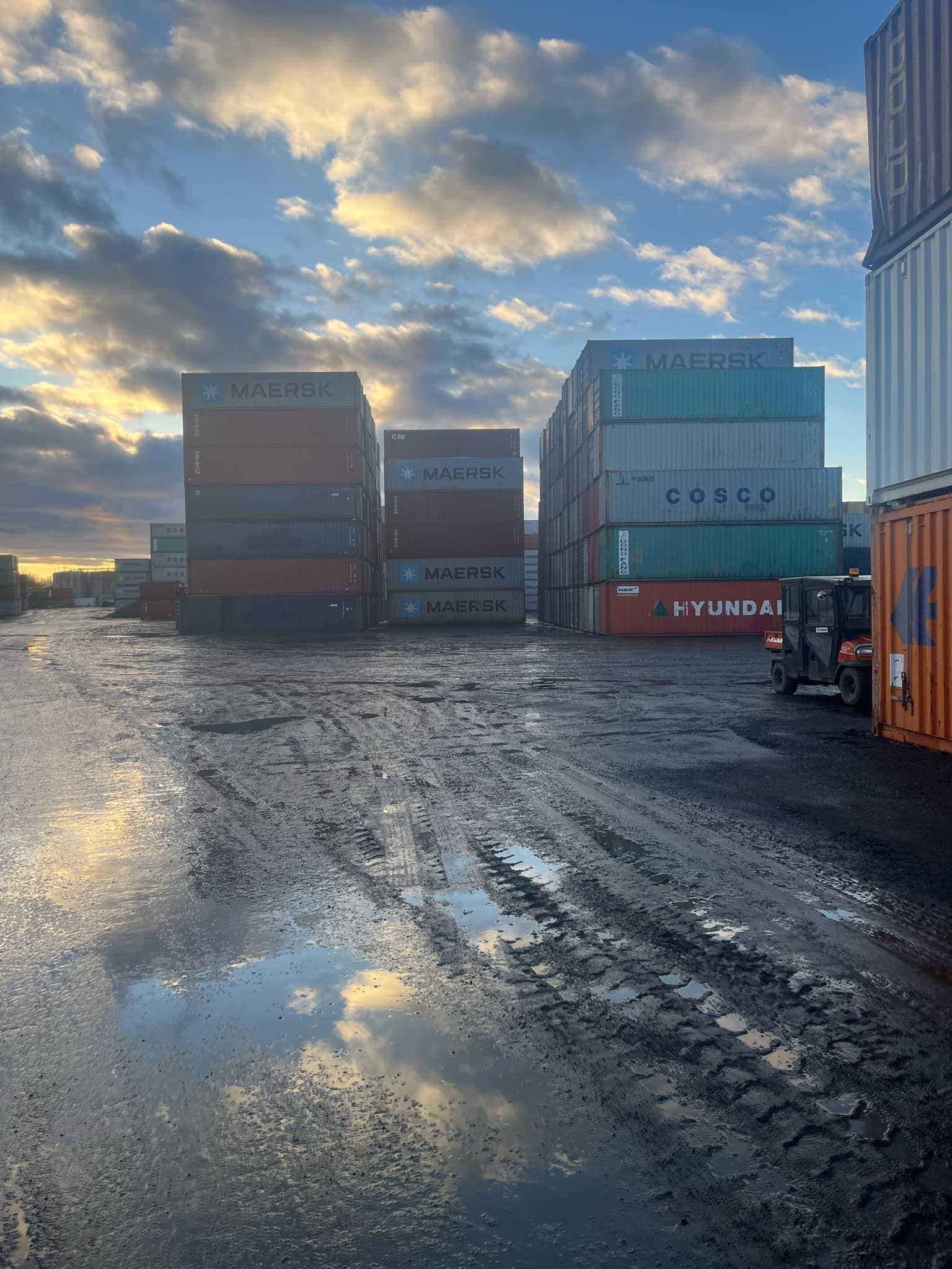 De nombreux conteneurs d'expédition sont empilés les uns sur les autres dans une zone boueuse.