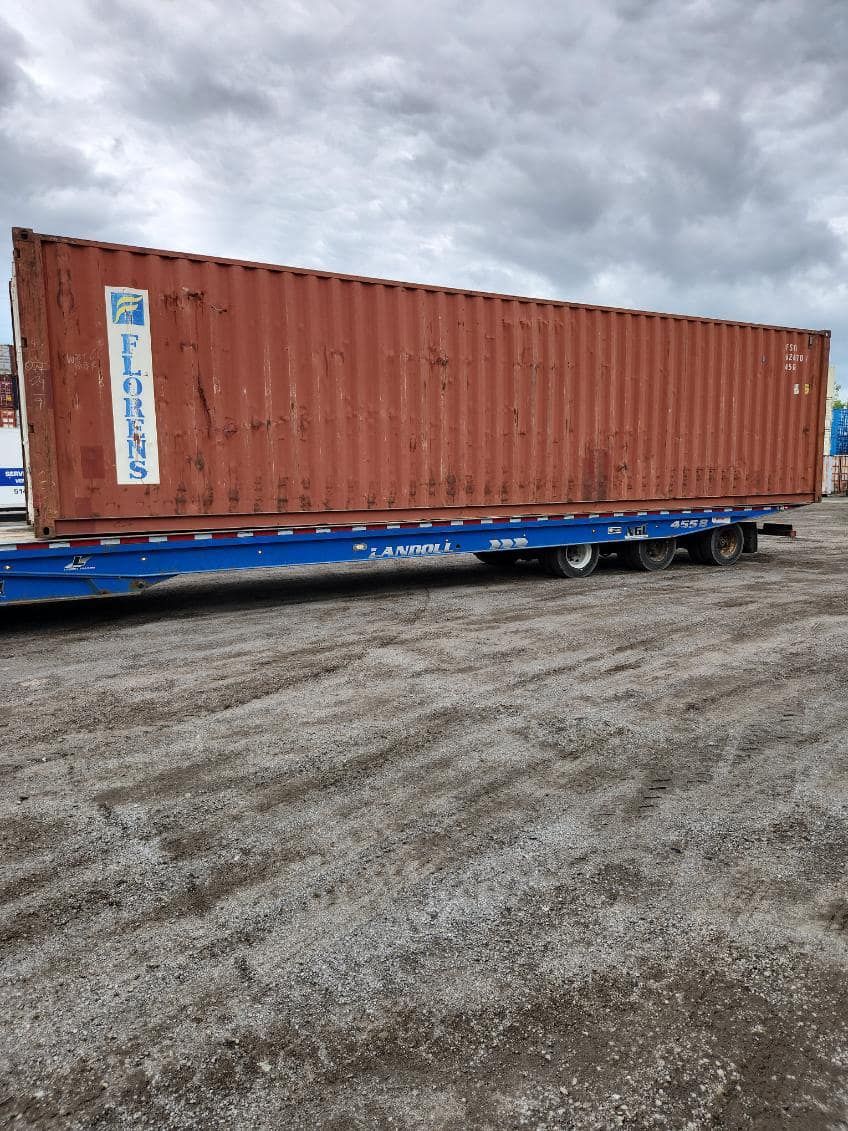 Un conteneur d'expédition rouge est posé sur une remorque bleue.