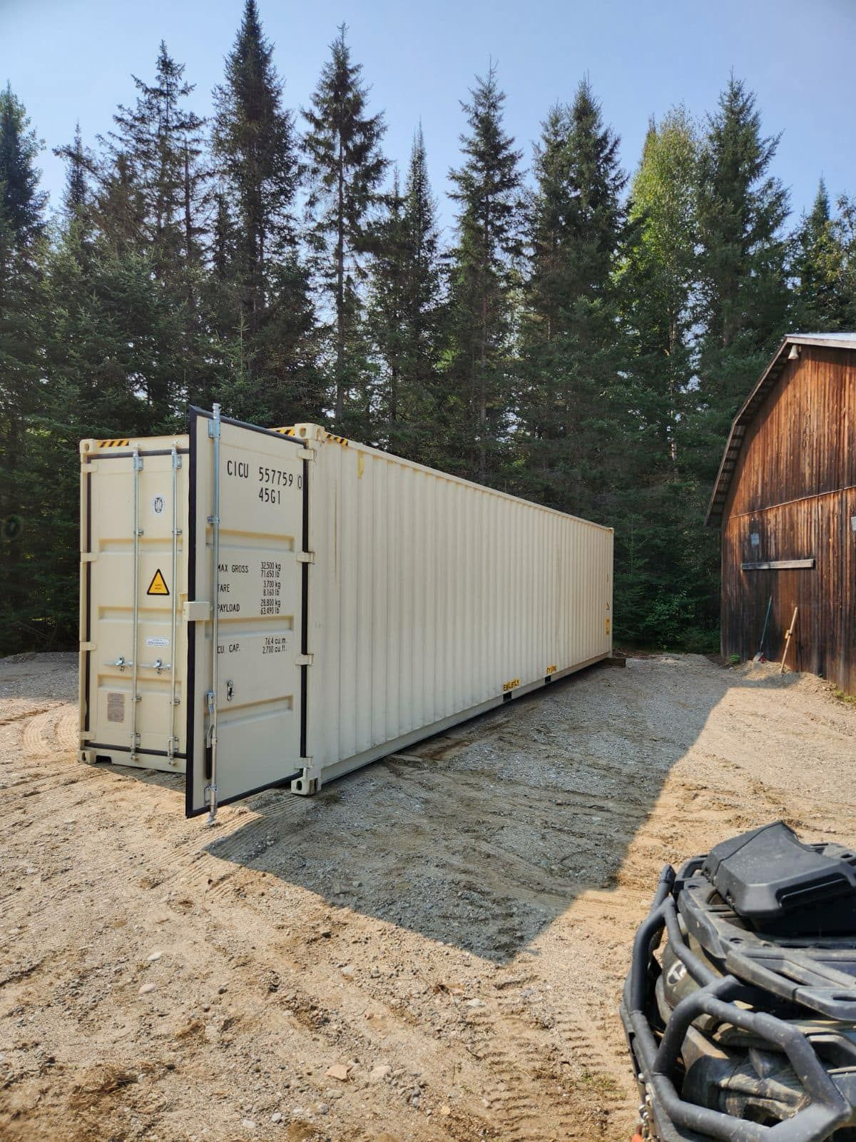 Un grand conteneur d'expédition est posé dans la terre devant un bâtiment en bois.