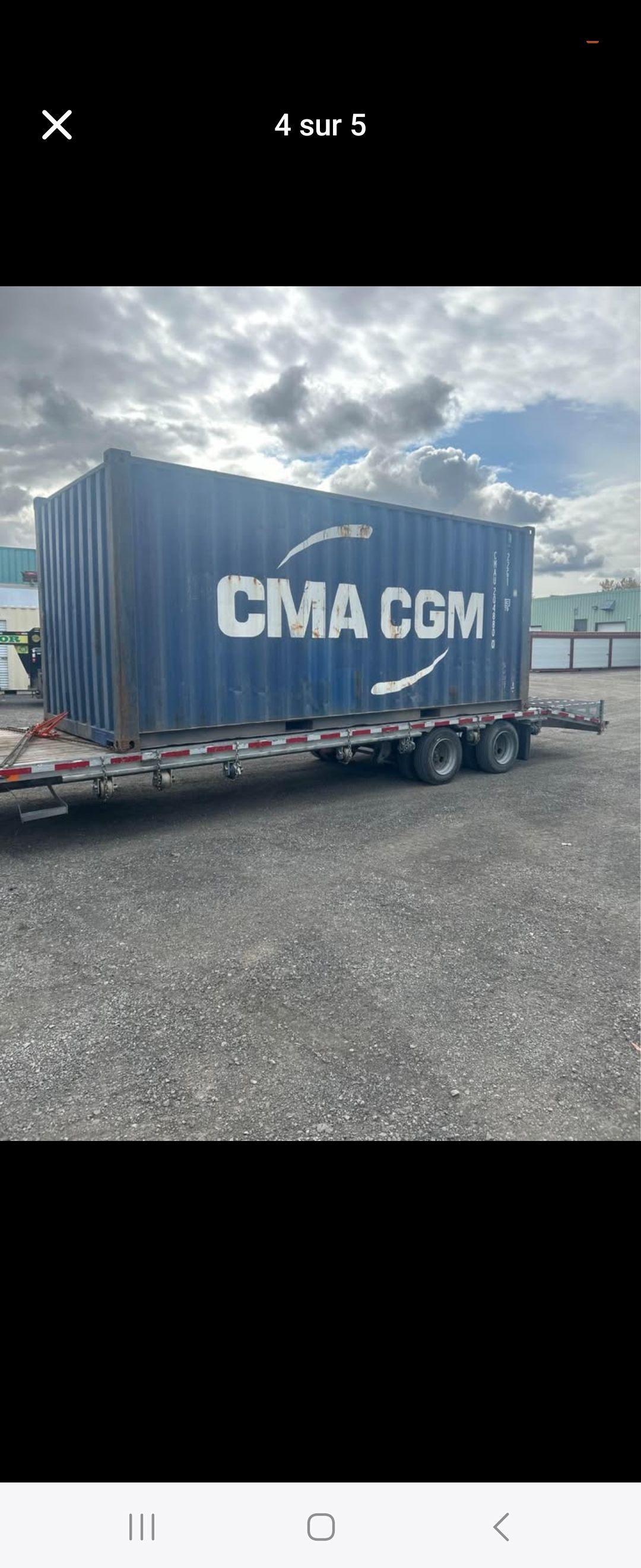 Un conteneur d'expédition bleu se trouve sur une remorque dans un parking.