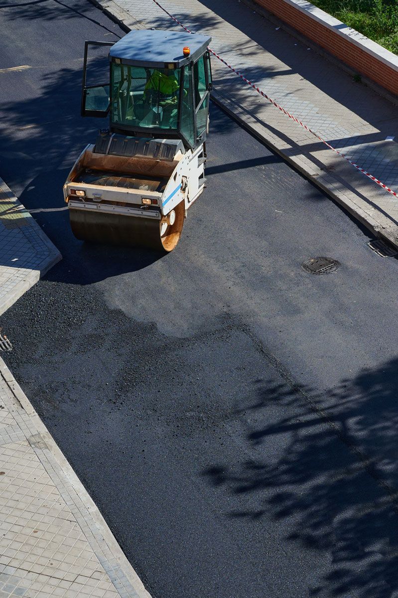 Road roller compacting fresh asphalt on a city street.