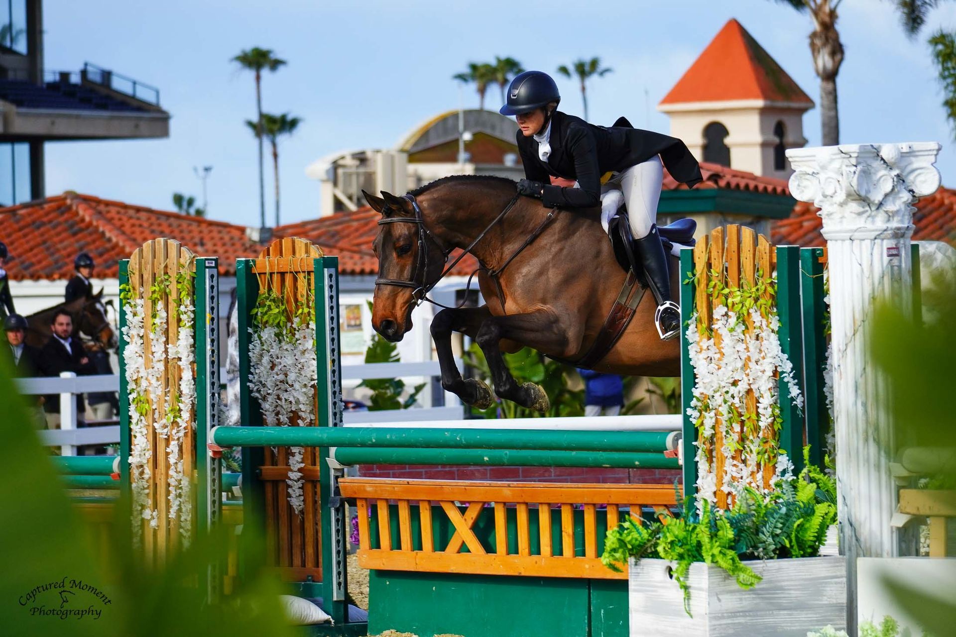 A person is riding a brown horse over a fence.