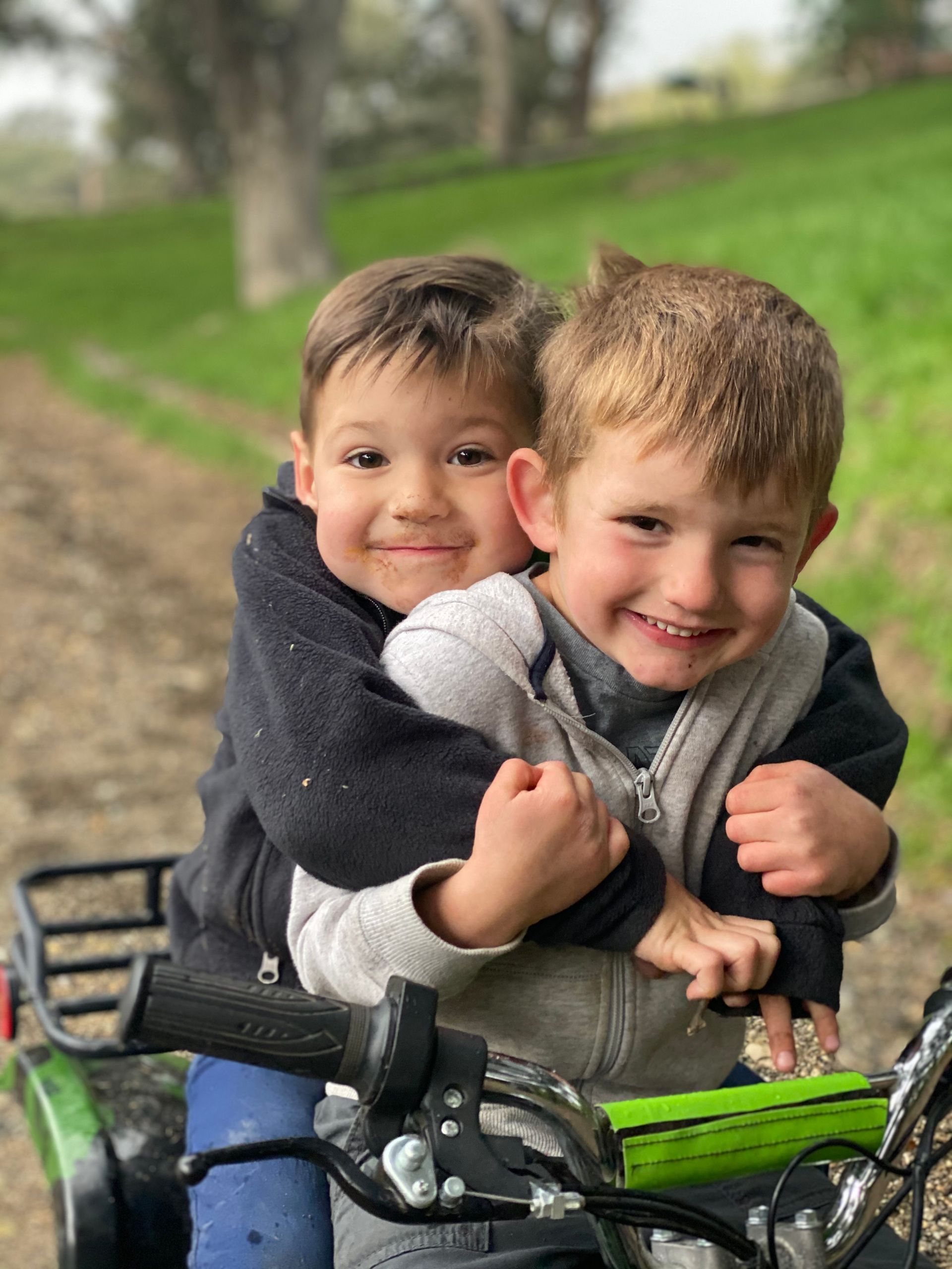 Two young boys are riding on the back of a four wheeler.