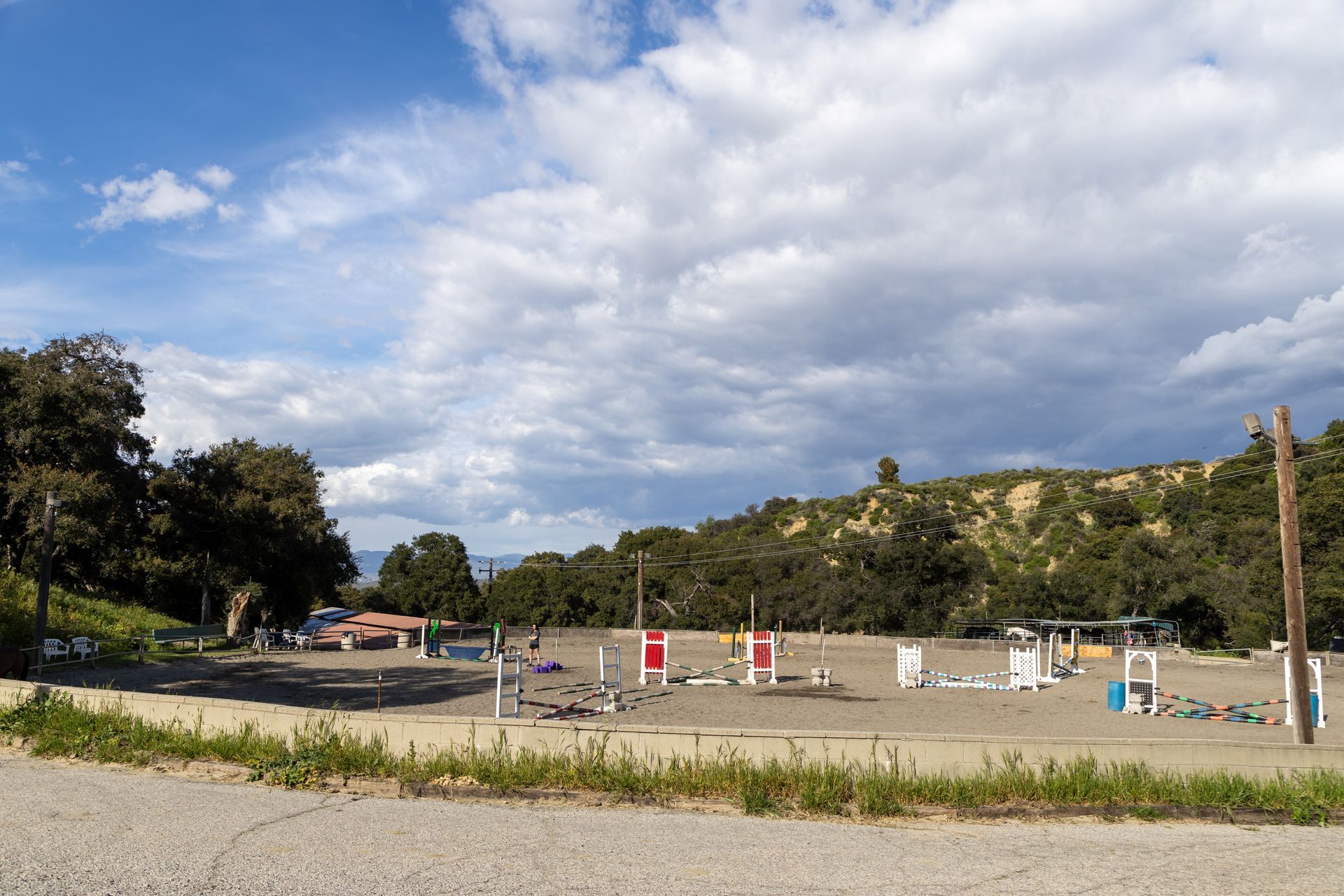 A dirt field with a lot of jumping fences and trees in the background.