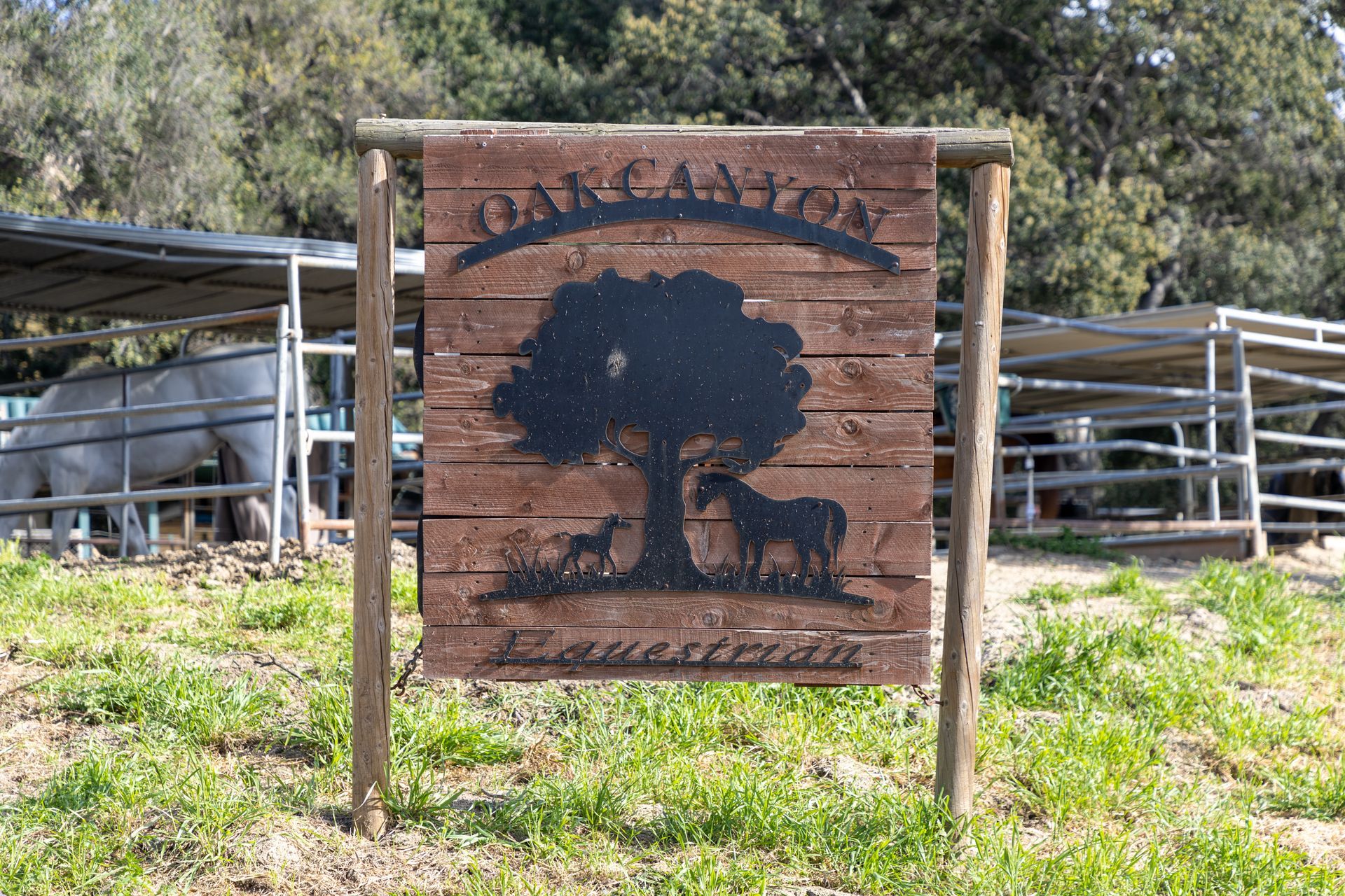 A wooden sign with a tree and horses on it is in a field.