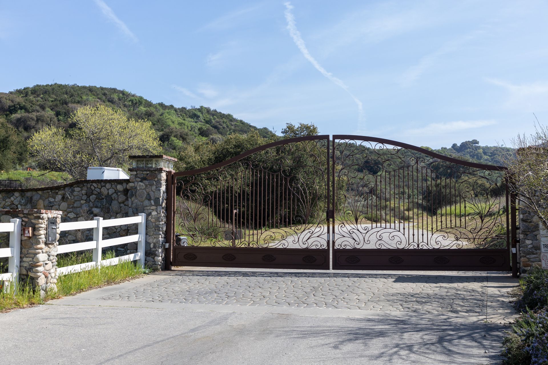 A large gate leading to a lush green field with mountains in the background.