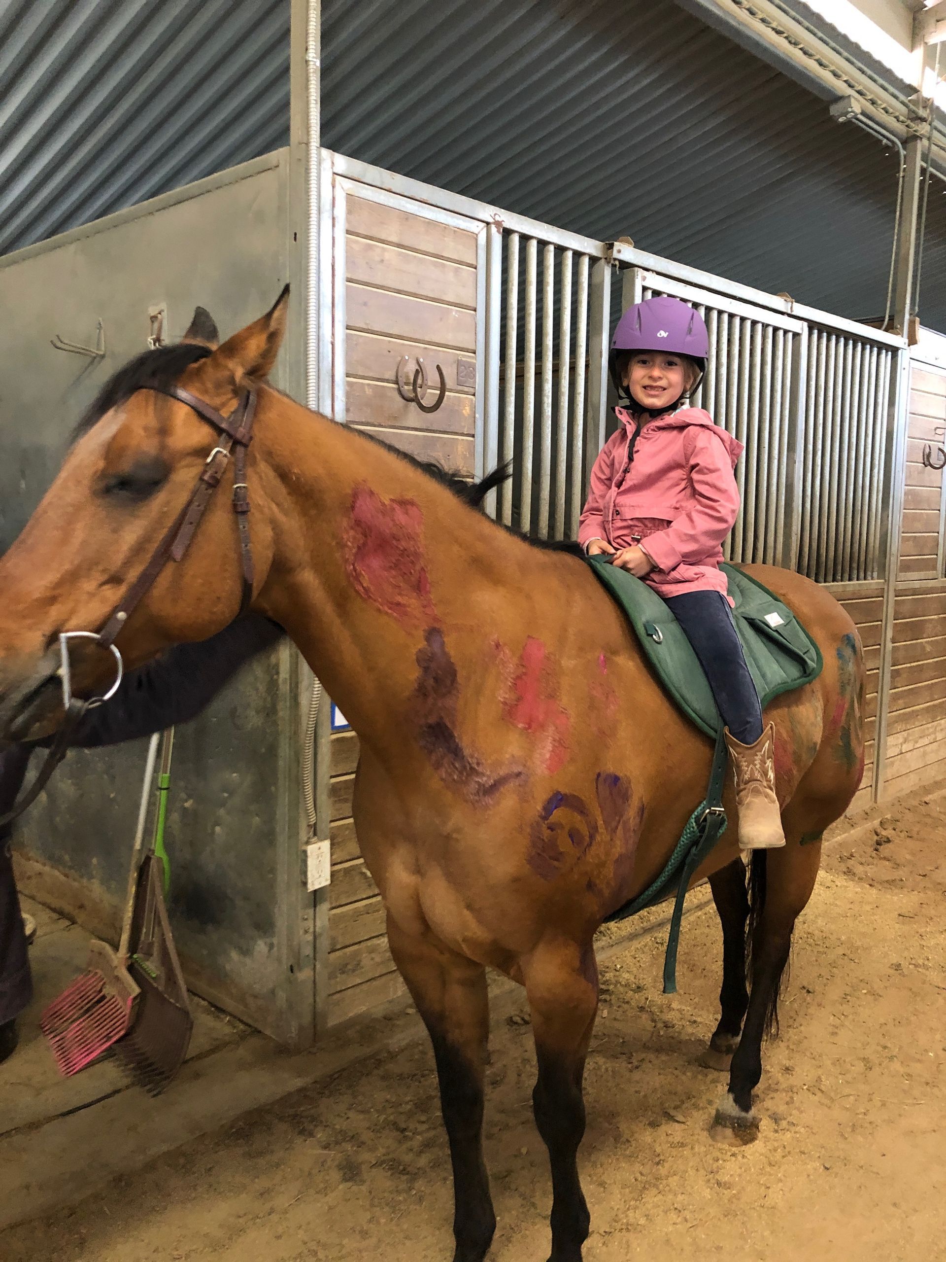 A little girl is riding a brown horse in a stable.