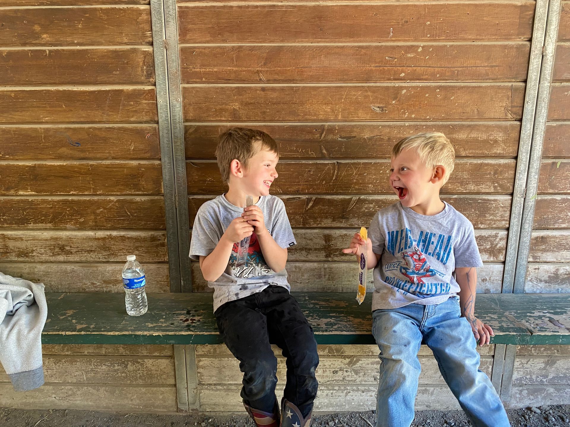 Two young boys are sitting on a bench eating ice cream.