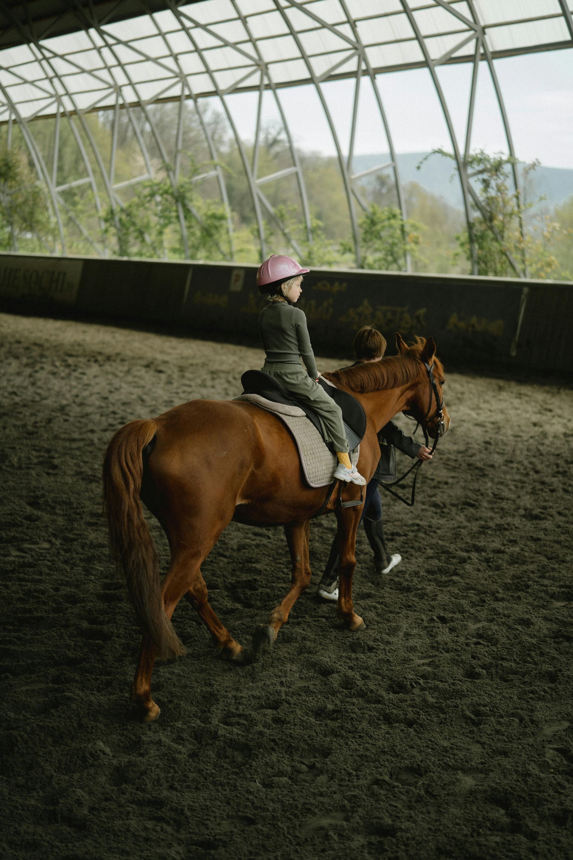 A young girl is riding a brown horse in an indoor arena.