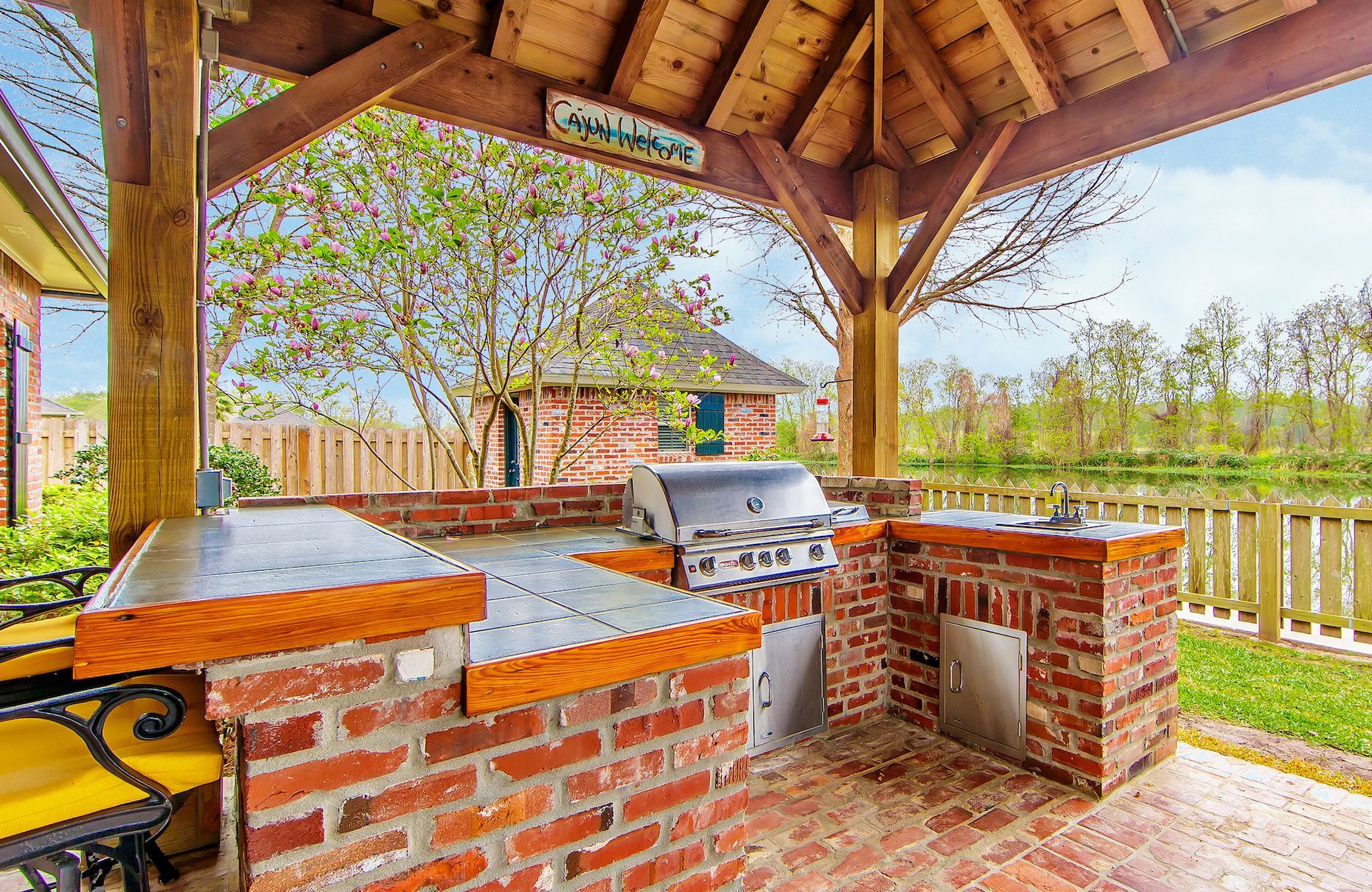 a brick outdoor kitchen with a grill under a wooden gazebo .