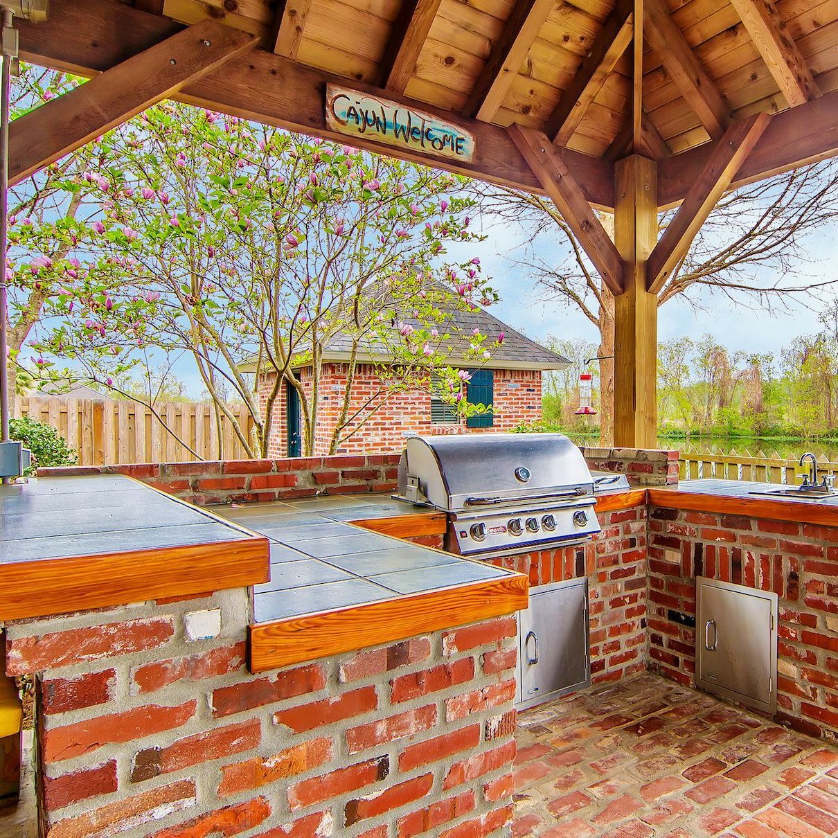 a brick outdoor kitchen with a grill under a wooden roof