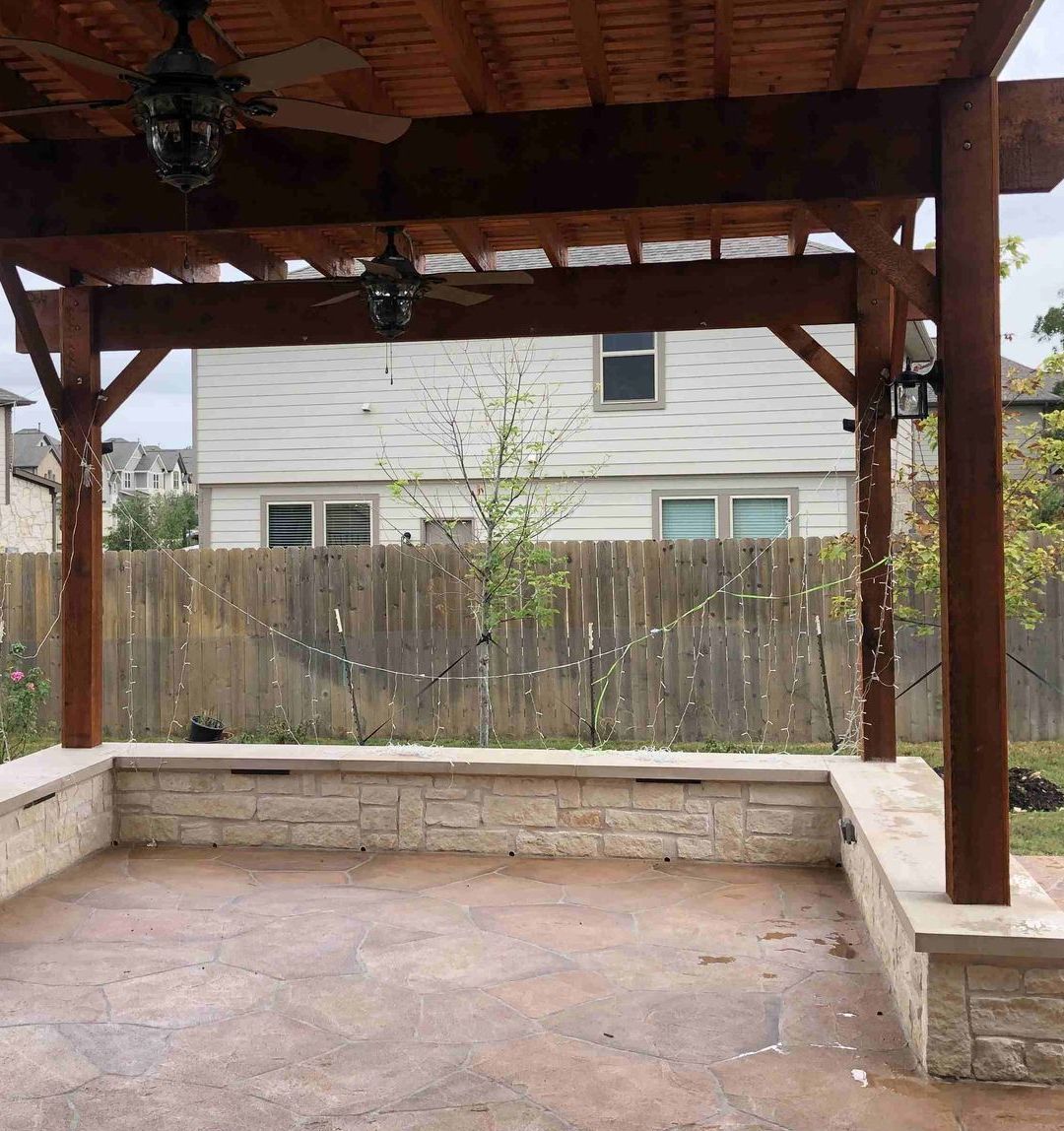 an empty patio with a wooden pergola and a wooden fence in the background .