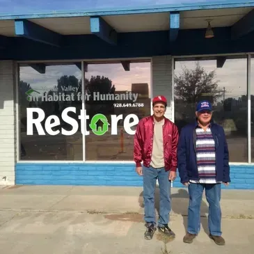 Two men standing in front of a building that says restore