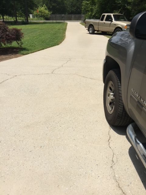 A gray pickup truck parked on a cracked concrete driveway, with a tan truck further up the drive.