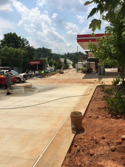 Gas station under construction; concrete work in progress. Red, white, and gray elements; people and vehicles present.