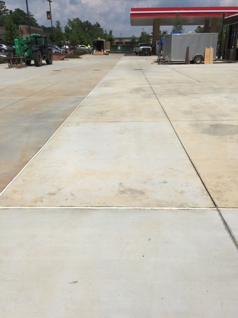 Concrete parking area with a gas station canopy in the background. A tractor is visible on the left side, with a trailer on the right.