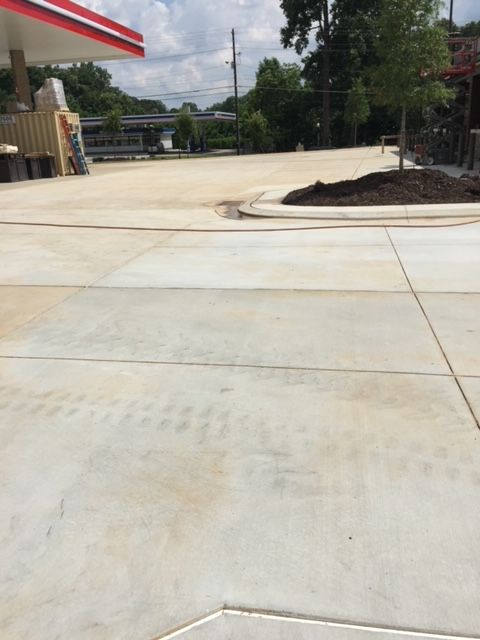View of a concrete parking area in front of a building with a red awning. Tire tracks are visible on the concrete.