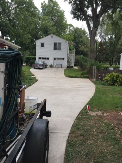 Pressure washer on driveway, partially cleaned. Garage and house in background, sunny day.