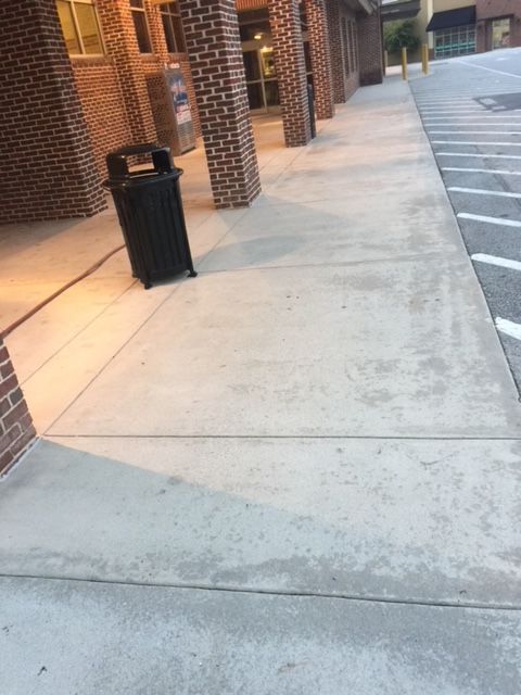 Sidewalk with brick pillars, a trash can, and building entrance. The concrete has water stains.