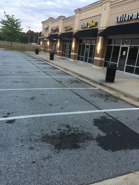 Empty parking lot in front of a strip mall with black awnings and brick accents; wet pavement, overcast sky.