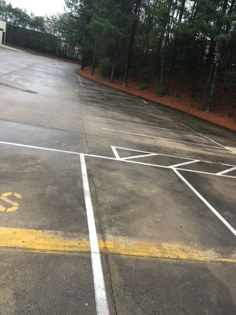 Wet, empty parking lot with white and yellow painted lines. Trees line the top and right side of the lot.