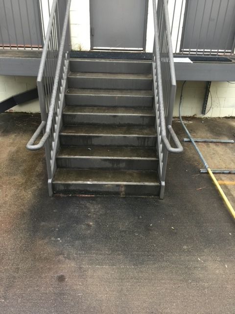 Exterior metal staircase leading to a door. The steps are wet, with handrails on both sides.