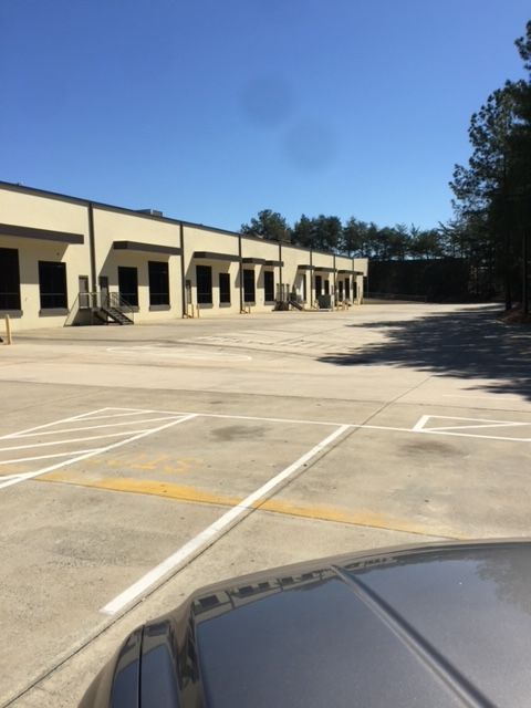 Exterior of a light industrial building with a large, empty parking lot on a sunny day.