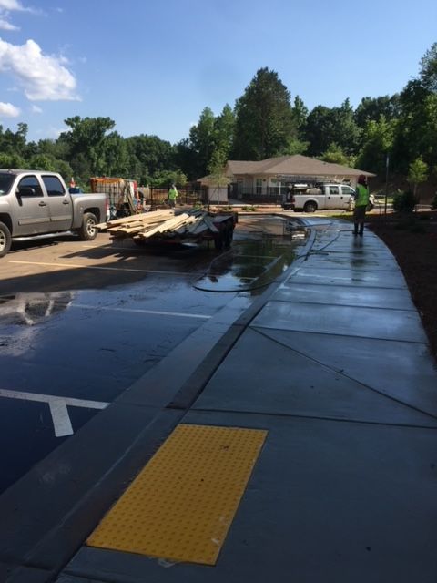 Newly poured concrete pathway with a yellow tactile warning. A truck and construction materials are in the parking lot, and trees are in the background.