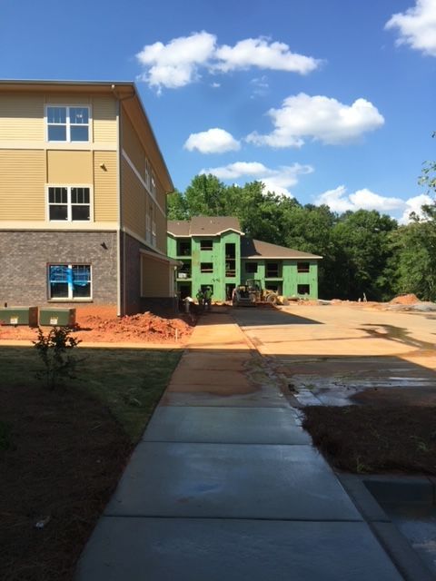 Construction site of multi-story buildings on a sunny day. Green, unfinished structures and a building with tan and brick exterior are visible.